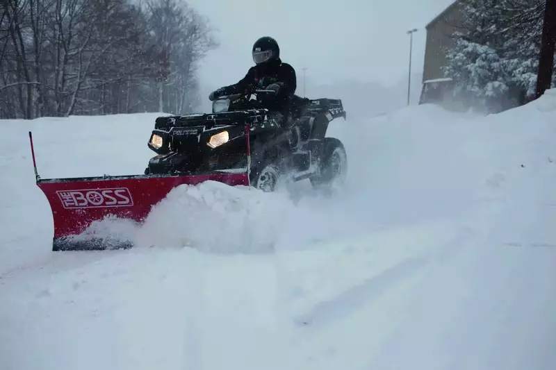 A person using an ATV equipped with a snow plow to clear a snowy driveway